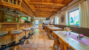 A wooden interior with a bar area, stools, tables, and a view through the window. - Gasthof Rafting Alm (Haiming)