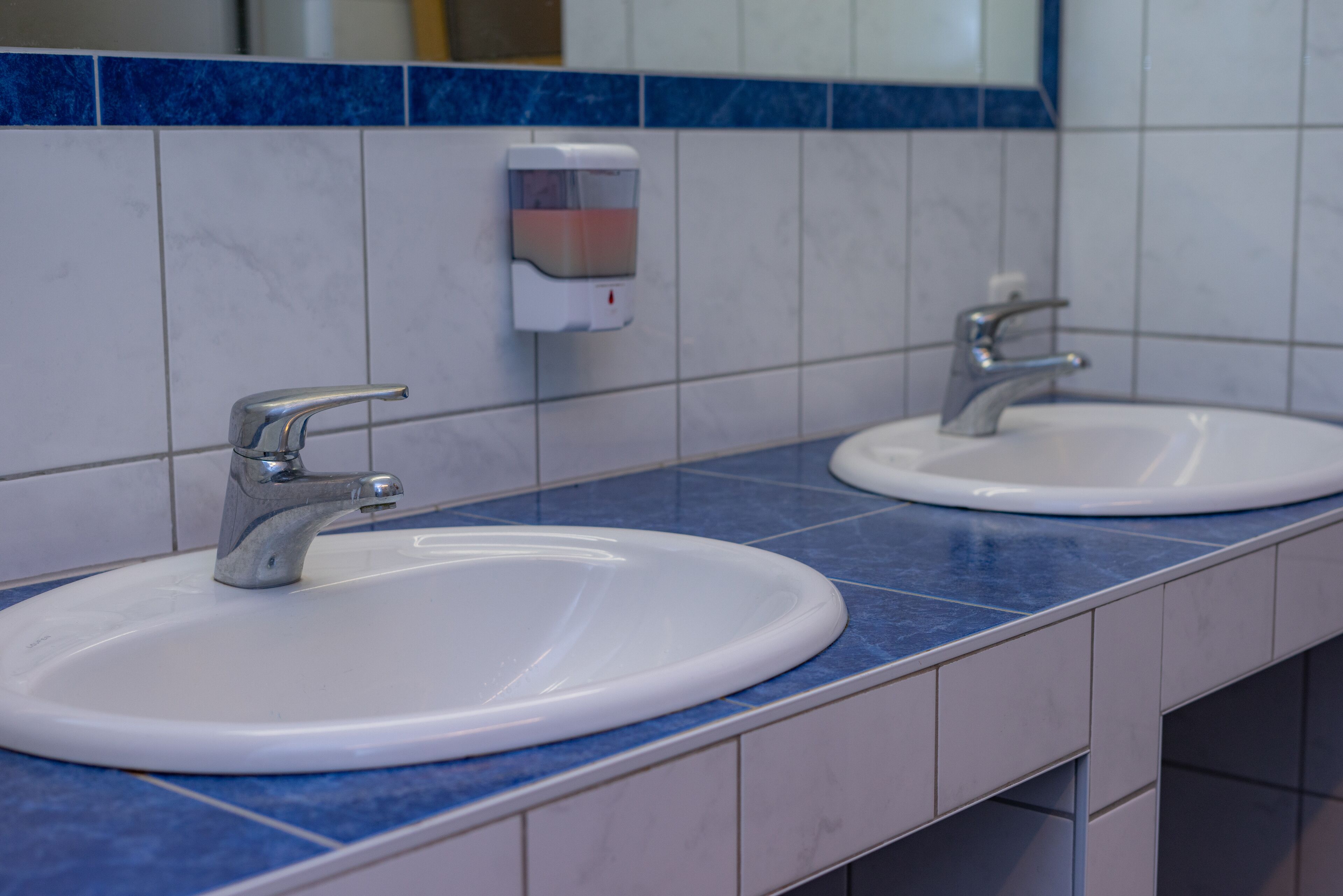 A bathroom with two sinks, a soap dispenser, and a mirror.