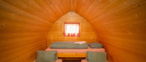 A cozy cabin room with two single beds, each with checkered bedding and pillows, and a small window with curtains.