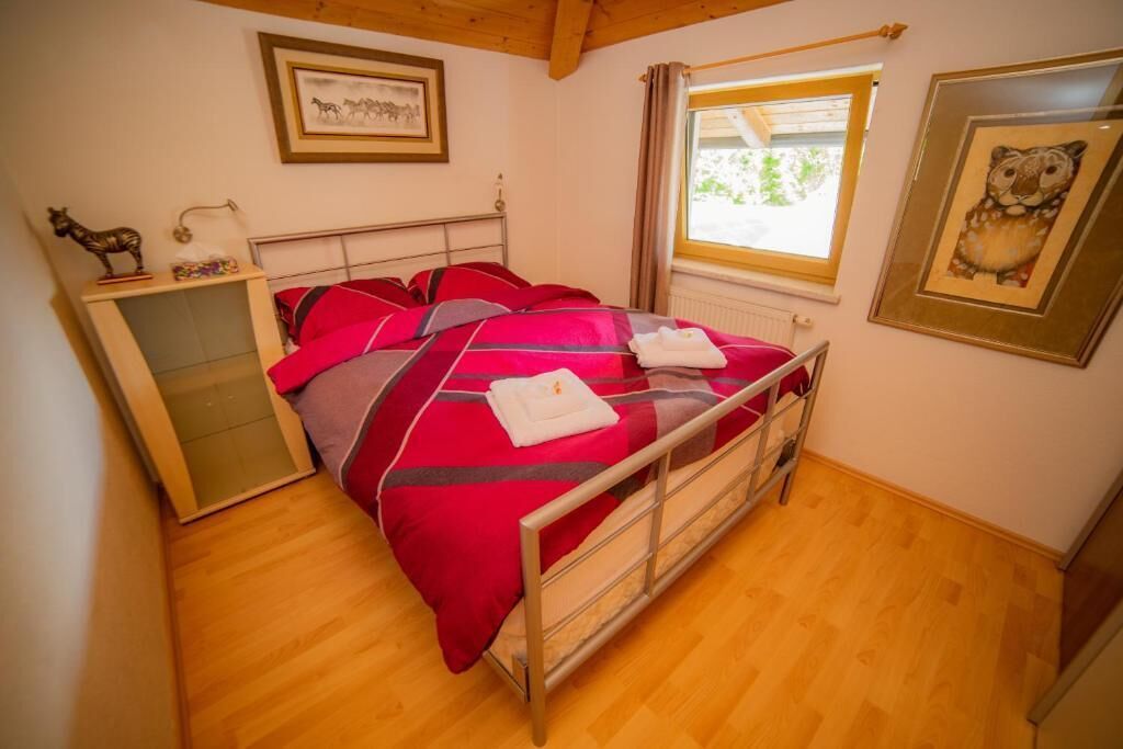 A single bed with red and gray bedding, a wooden dresser, and a window with curtains.