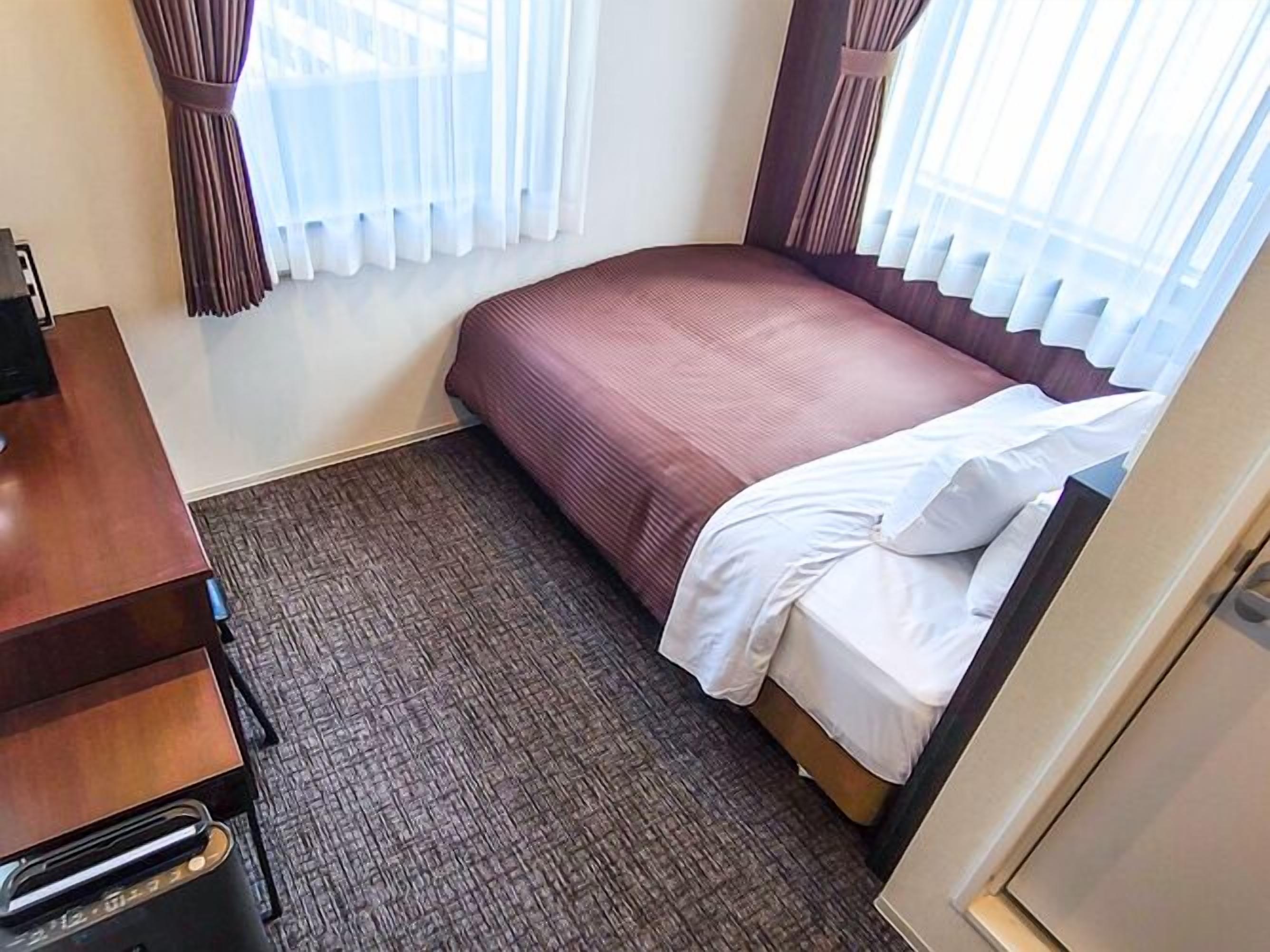 A hotel room with a bed, a desk, and a window with curtains.