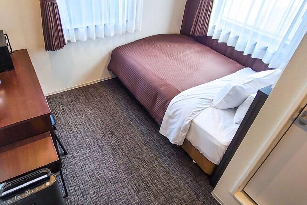 Una habitación de hotel con una cama, un escritorio y un ventanal con cortinas.