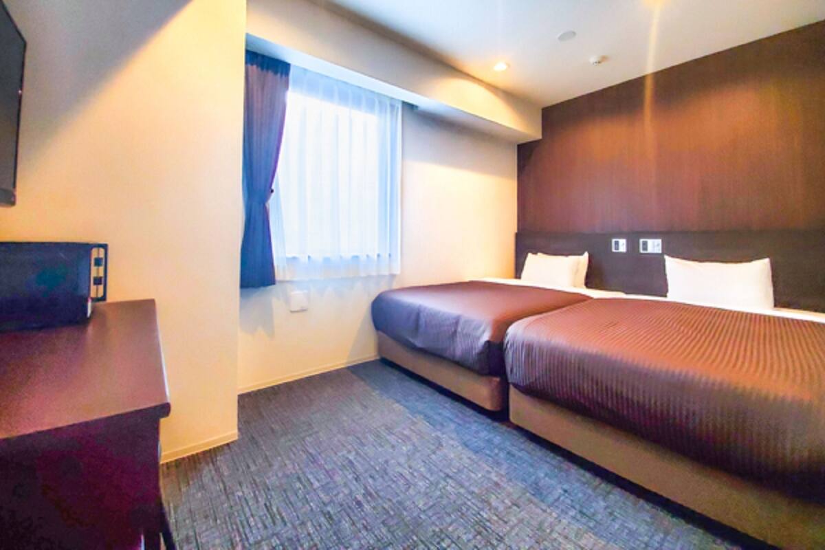 Habitación de hotel con dos camas, un escritorio, una ventana con cortinas y piso alfombrado.