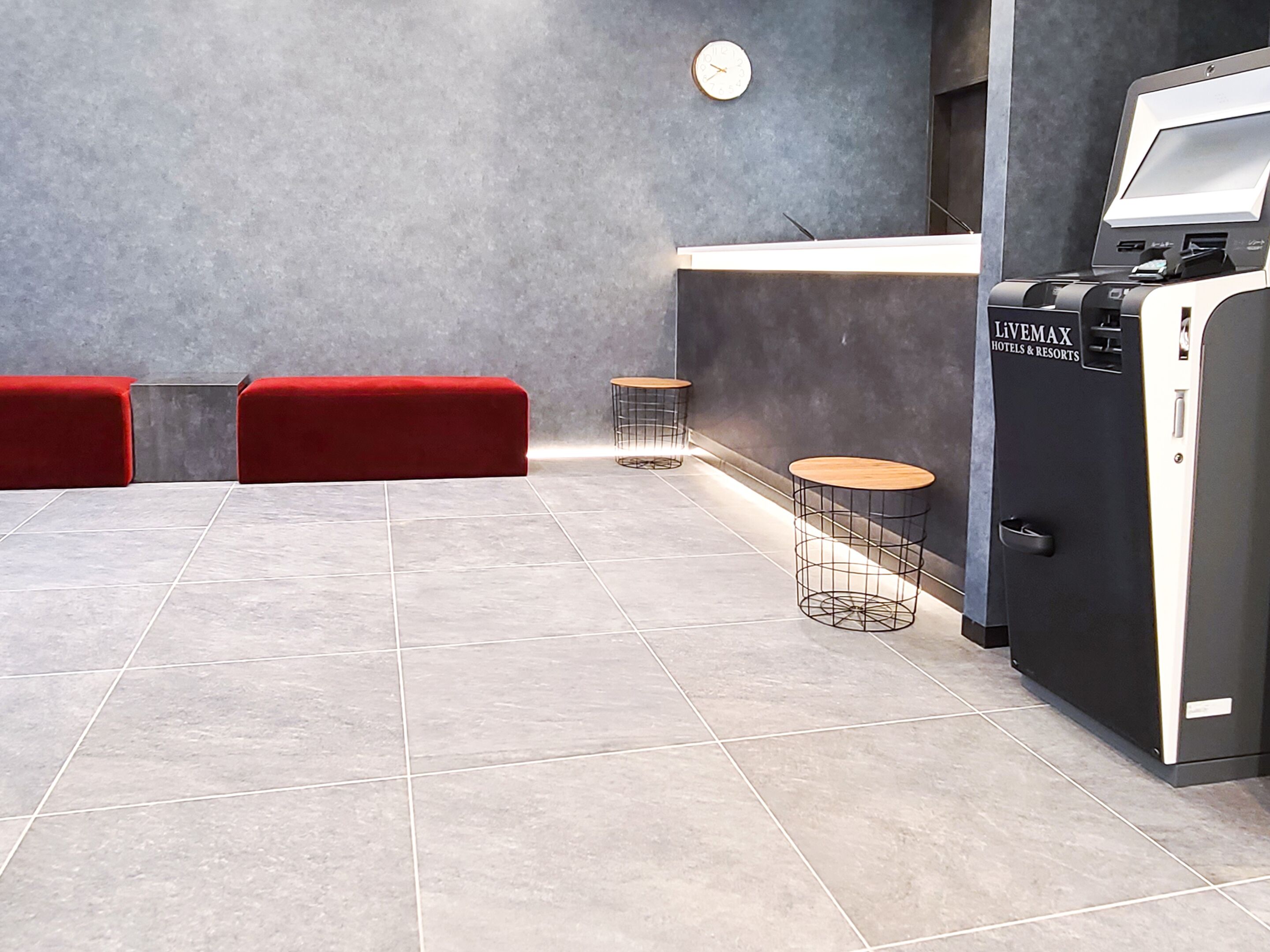 Un moderno vestíbulo de hotel con mostrador de recepción, un reloj, asientos rojos y un minibar.