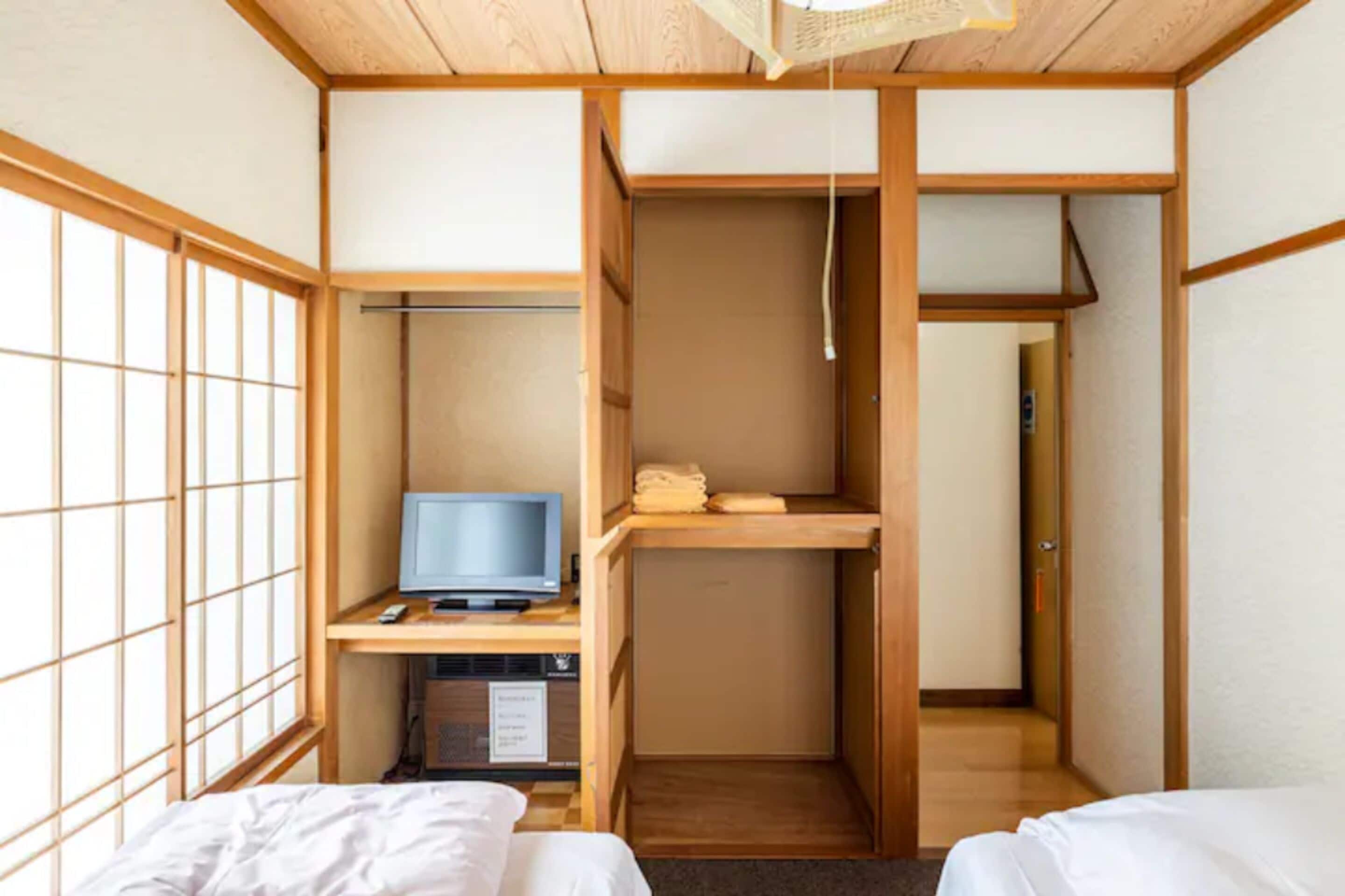 A traditional Japanese-style room with tatami flooring, a futon bed, a television on a low wooden table, and a sliding door leading to another room.