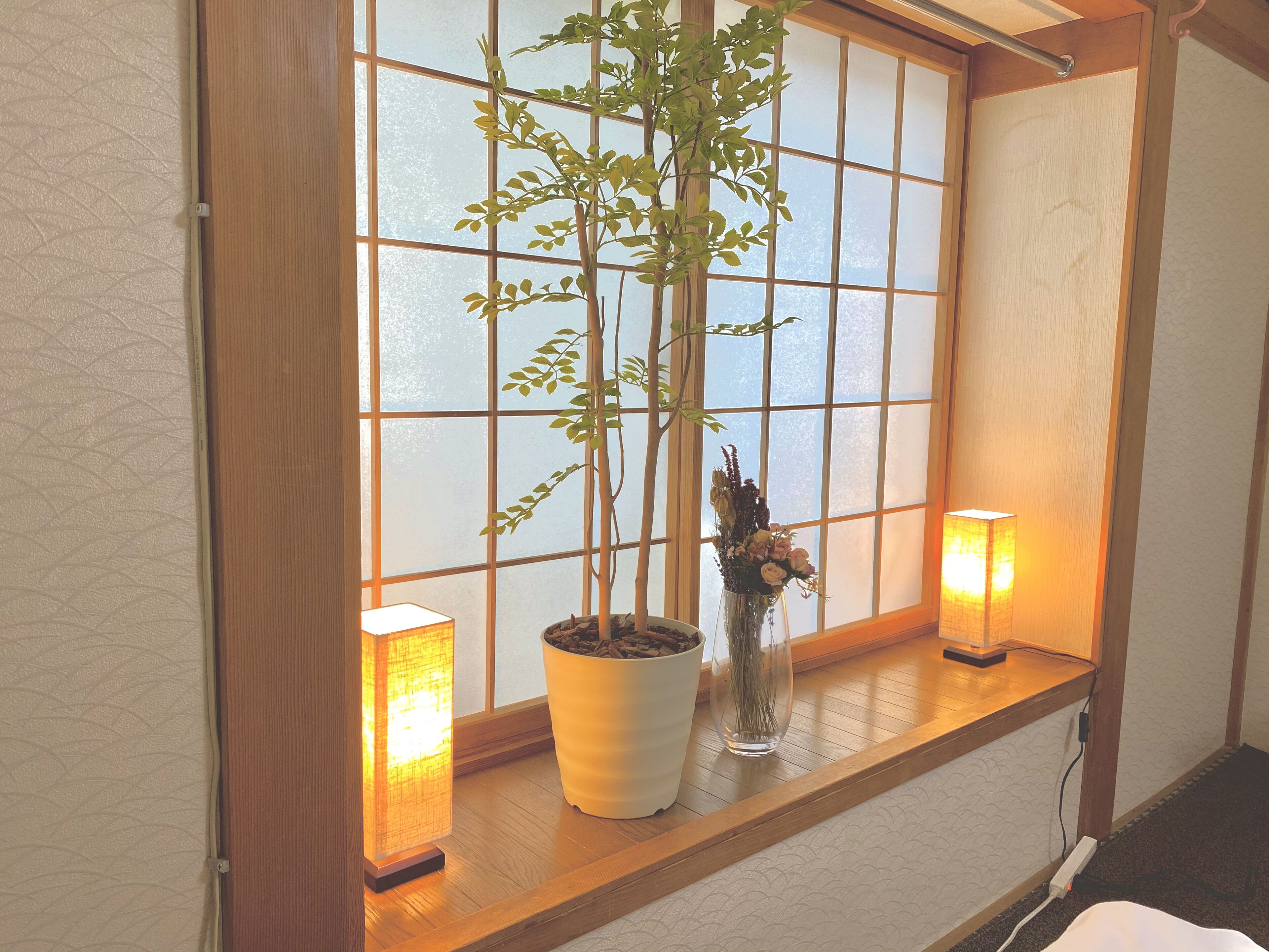 A room with a wooden window sill, a potted plant, and two wall-mounted lamps.