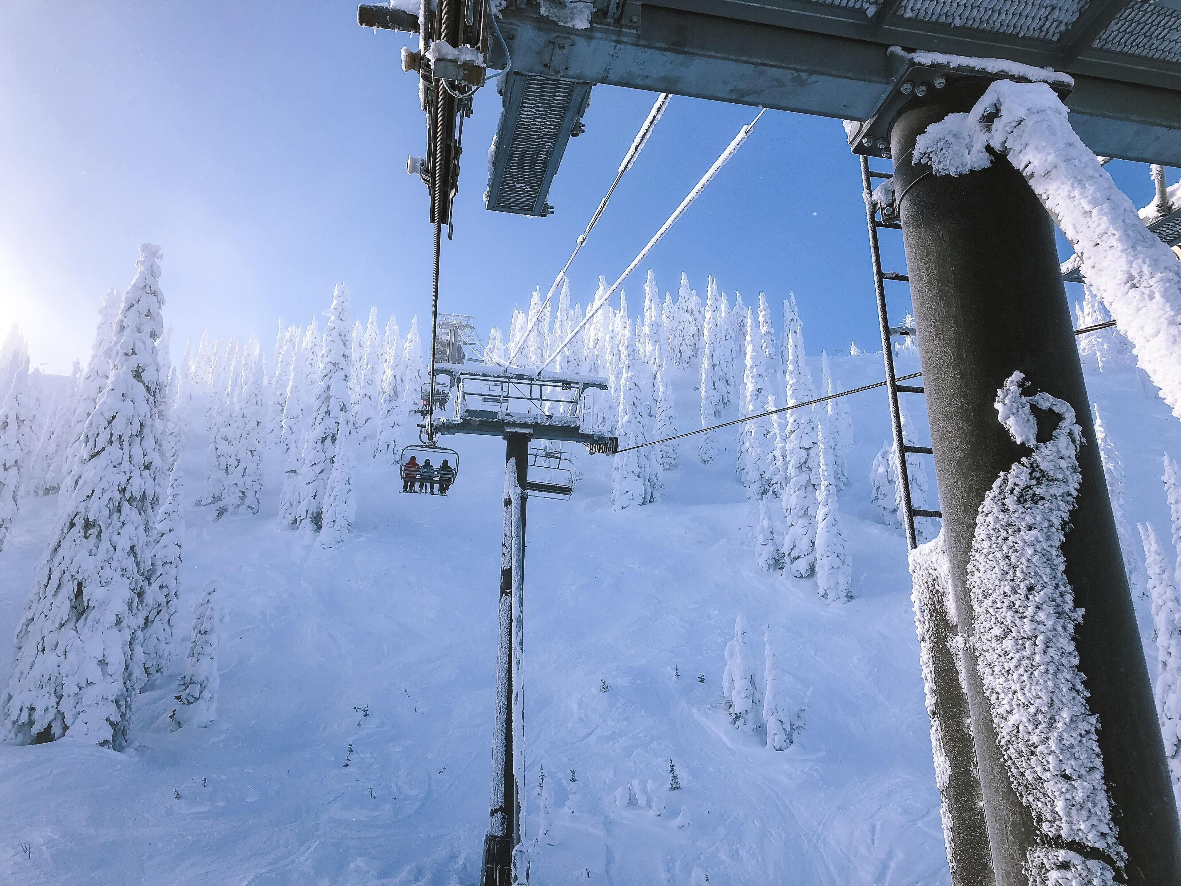 A ski lift chair suspended over a snowy landscape with snow-covered trees.