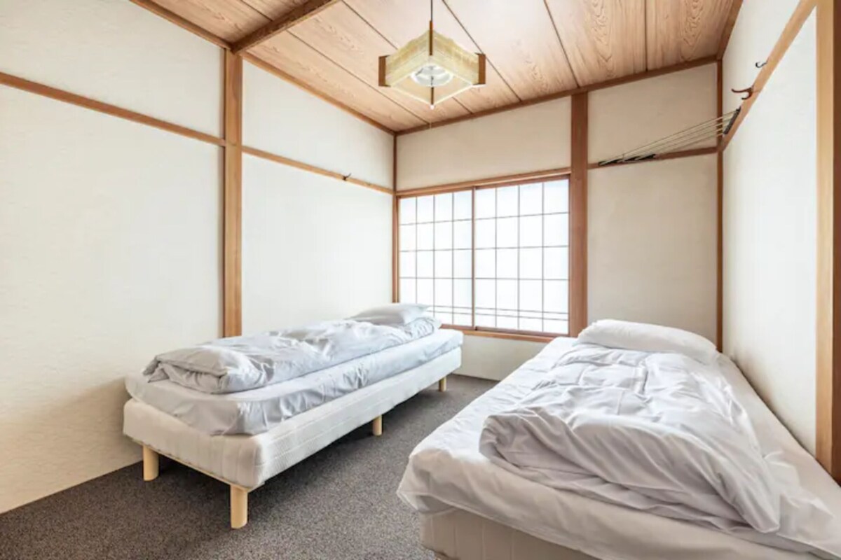 Una habitación con dos camas individuales, techo de madera y un ventanal grande.