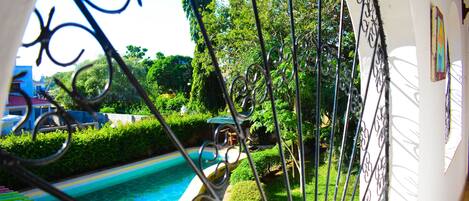 Une piscine entourée de verdure et un bâtiment blanc doté d’un balcon.