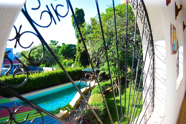 A view of a swimming pool surrounded by greenery and a white building with a balcony.