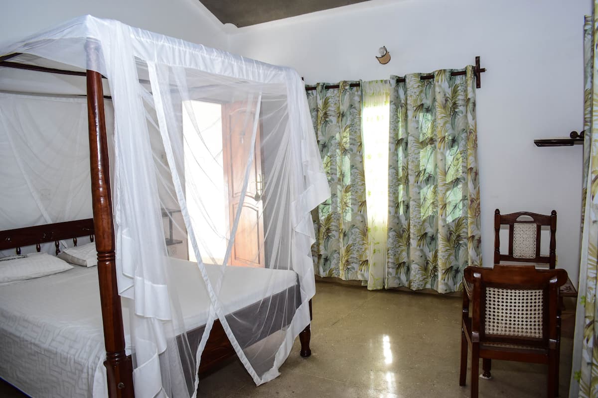 Une chambre avec un lit à baldaquin muni d’une moustiquaire, une chaise en bois et une fenêtre avec des rideaux.