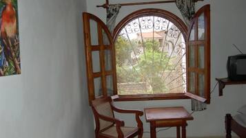 A room with a wooden-framed window, a chair, a small table, and a television.