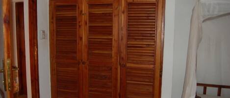 A room with a wooden wardrobe, a bed with a white canopy, and a white wall.