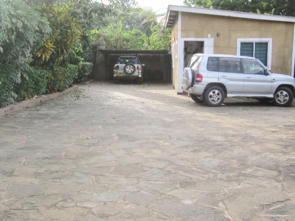 Um caminho de paralelepípedos leva a um edifício, onde se vê um SUV e um carro estacionados.