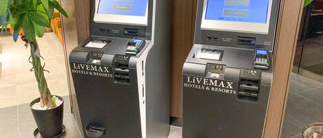 Två självbetjäningskiosker från LiVEMAX Hotels & Resorts, utrustade med kortbetalningsfunktion och en kvittskrivare.