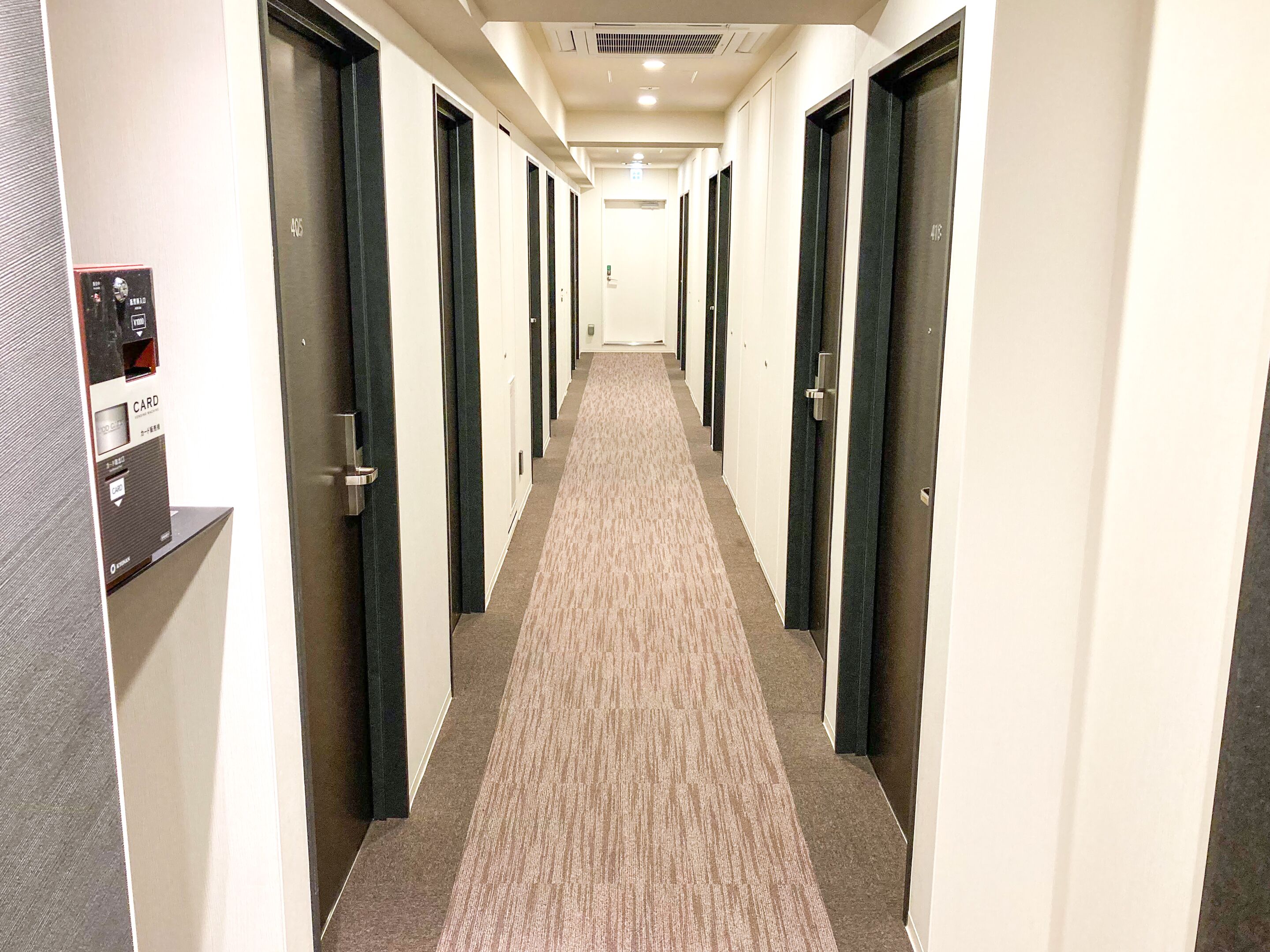 A hotel corridor with multiple doors, a card reader, and a carpeted floor.