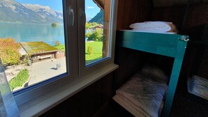 A room with a window overlooking a lake and mountains, a bunk bed, and a small outdoor seating area. - Lake Lodge Hostel (Iseltwald)