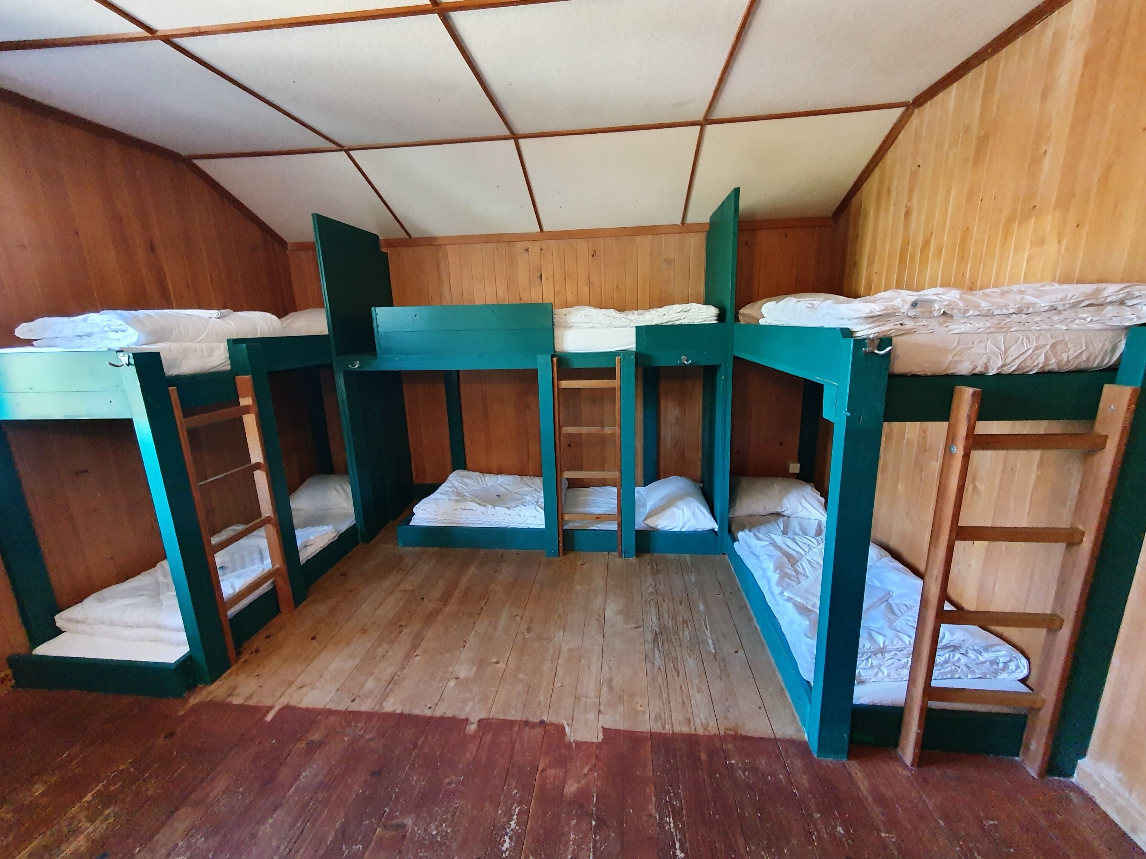 A dormitory room with bunk beds, wooden walls, and a tiled ceiling.