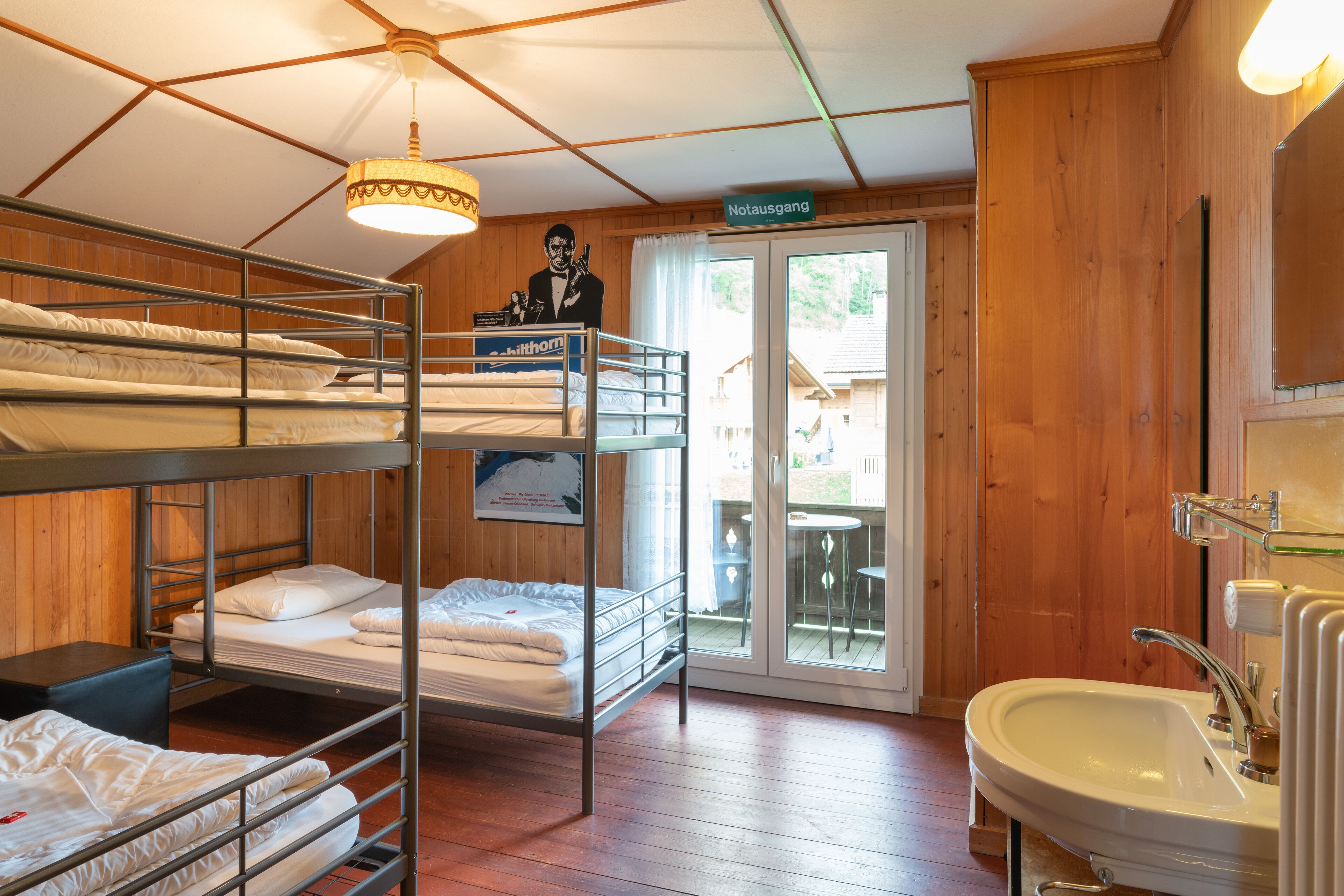 Habitación con literas, escritorio, silla, lavamanos y un cartel en la pared.