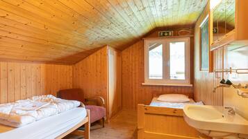 Une pièce de cabane en bois comprenant deux lits, une chaise, une fenêtre et un lavabo.