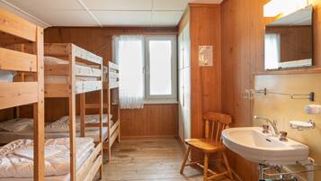 Una cabaña de madera con literas, una silla de madera y un lavabo con espejo.