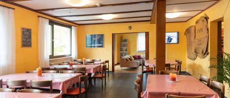 Un restaurante con varias mesas y sillas, paredes amarillas y un televisor en la pared.