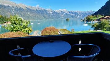 Una terraza con una mesa redonda y dos sillas, con vistas a un lago con barcos y montañas al fondo.