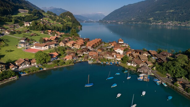 A lakeside village with traditional buildings, boats, and mountains in the background. - Lake Lodge Hostel (Iseltwald)