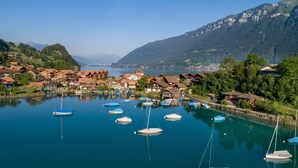 A lakeside village with traditional houses, boats, and mountains in the background. - Lake Lodge Hostel (Iseltwald)