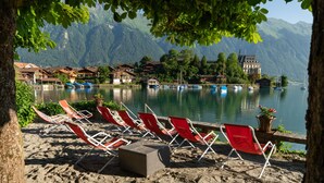 A lakeside view with red lounge chairs and a historic building in the background. - Lake Lodge Hostel (Iseltwald)