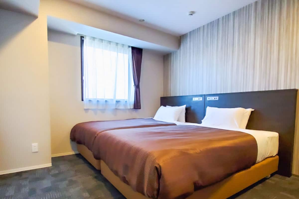 A hotel room with a large bed, a window with curtains, and a headboard with controls.