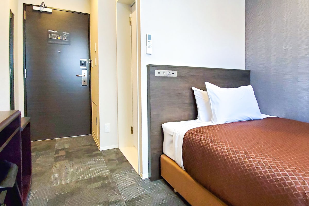 A hotel room with a bed, a desk, and a door.
