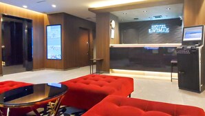 A hotel reception area with a digital display, a reception desk, and red seating. - HOTEL LiVEMAX Tachikawa Ekimae (Tachikawa)