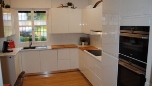 A modern kitchen with white cabinets, wooden countertops, a built-in oven, and a window with a view of greenery. - Exclusive villa with garden, sauna and forest access  (Solingen)