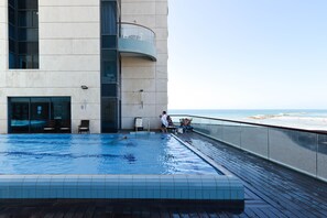 A swimming pool with a view of the beach, a glass balustrade, and a few lounge chairs. - Deluxe 2 Bedroom Apartment in Herzylia (Herzliya)