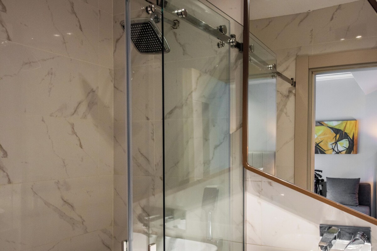 A modern bathroom with a glass-enclosed shower, a white sink, and a marble-tiled floor.