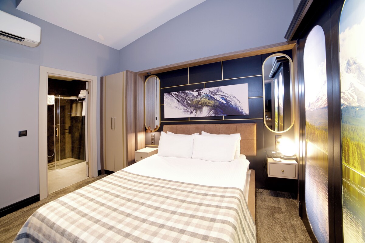 A hotel room with a large bed, a bathroom with a glass door, and a wall-mounted TV.