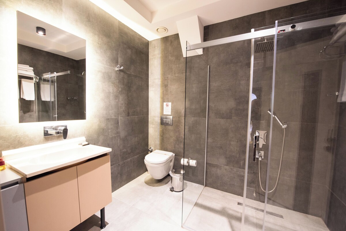 Un bany modern amb plat de dutxa inclòs en vidre, un vàter i un lavabo amb mirall.