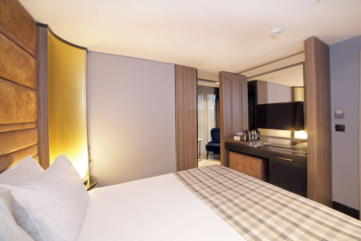 A hotel room with a bed, a desk, a chair, a television, and a bathroom visible through a door.
