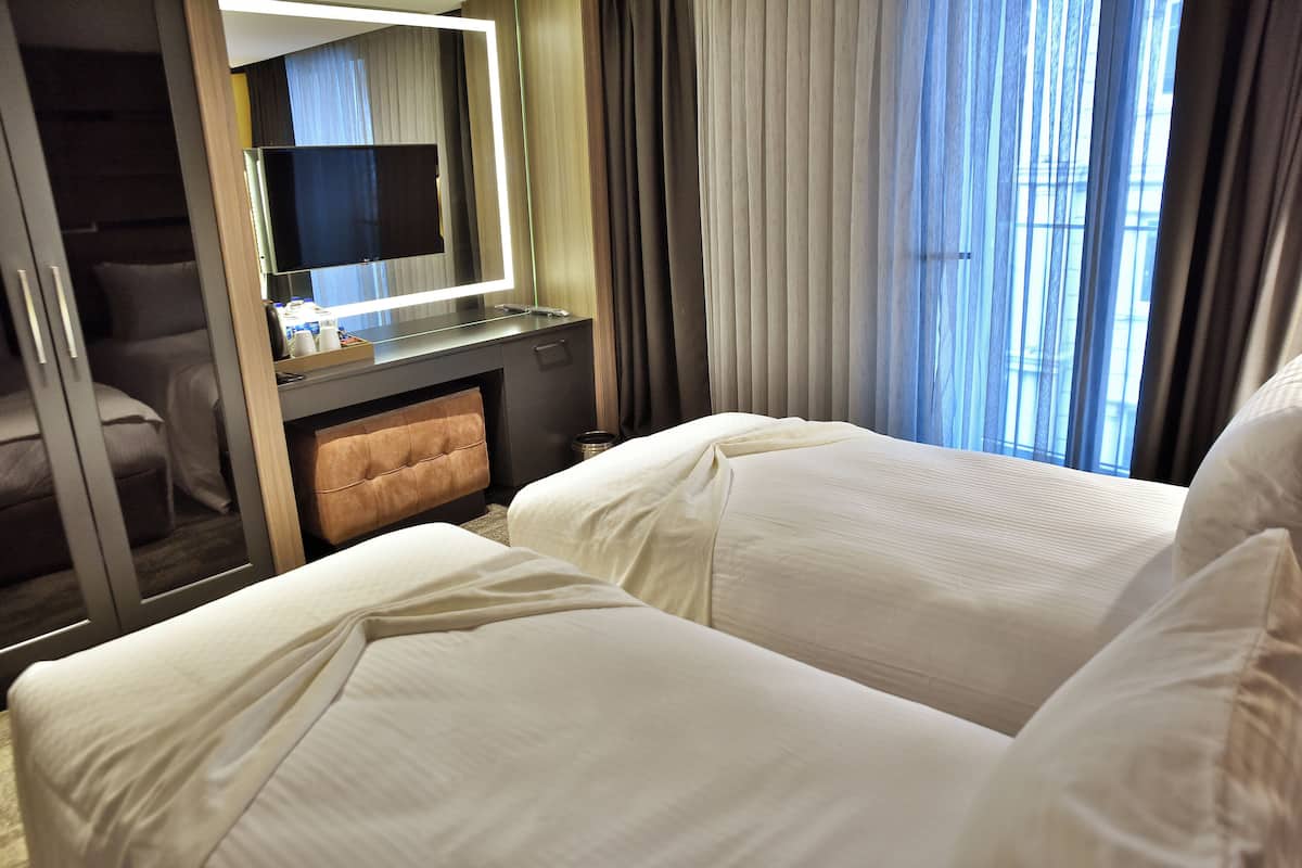 A hotel room with two beds, a vanity with a mirror, and a view of the outdoors through large windows.