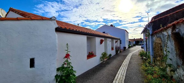 A narrow street with white buildings, red-tiled roofs, and small windows.