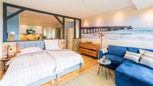 Un dormitorio moderno con una cama grande, un sofá azul y vista al océano a través de una ventana.