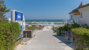 Un paseo marítimo que conduce a una playa con una torre de salvavidas y un cartel.