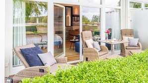 Un espacio exterior moderno con mobiliario de mimbre, un ventanal de vidrio que da a una cocina y vistas al jardín.