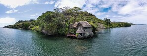 A thatched-roof hut on a small island surrounded by water, with lush greenery and a clear sky. - Mfangano Island Lodge (Mfangano Island)