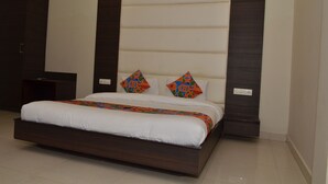 A modern bedroom with a large bed, dark wood headboard, and colorful geometric pillows. - Hotel KK Continental (Amritsar)