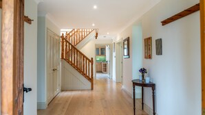 A hallway with a wooden staircase, a dining area, and a kitchen in the background. - Wonderful Spacious Family Home in Constantine Bay Situated on Road to Beach (Constantine Bay)