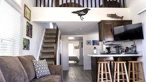 Una cocina moderna con un televisor de pantalla plana, taburetes de madera y una escalera que lleva a una zona superior con una decoración de pájaros y peces.