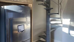 Una cuina amb nevera d'acer inoxidable, forn integrat i una escala moderna amb barana de vidre.