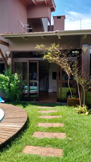 Een huis met een overdekte patio, een houten terras en een gazon met staptegels die naar de ingang leiden.
